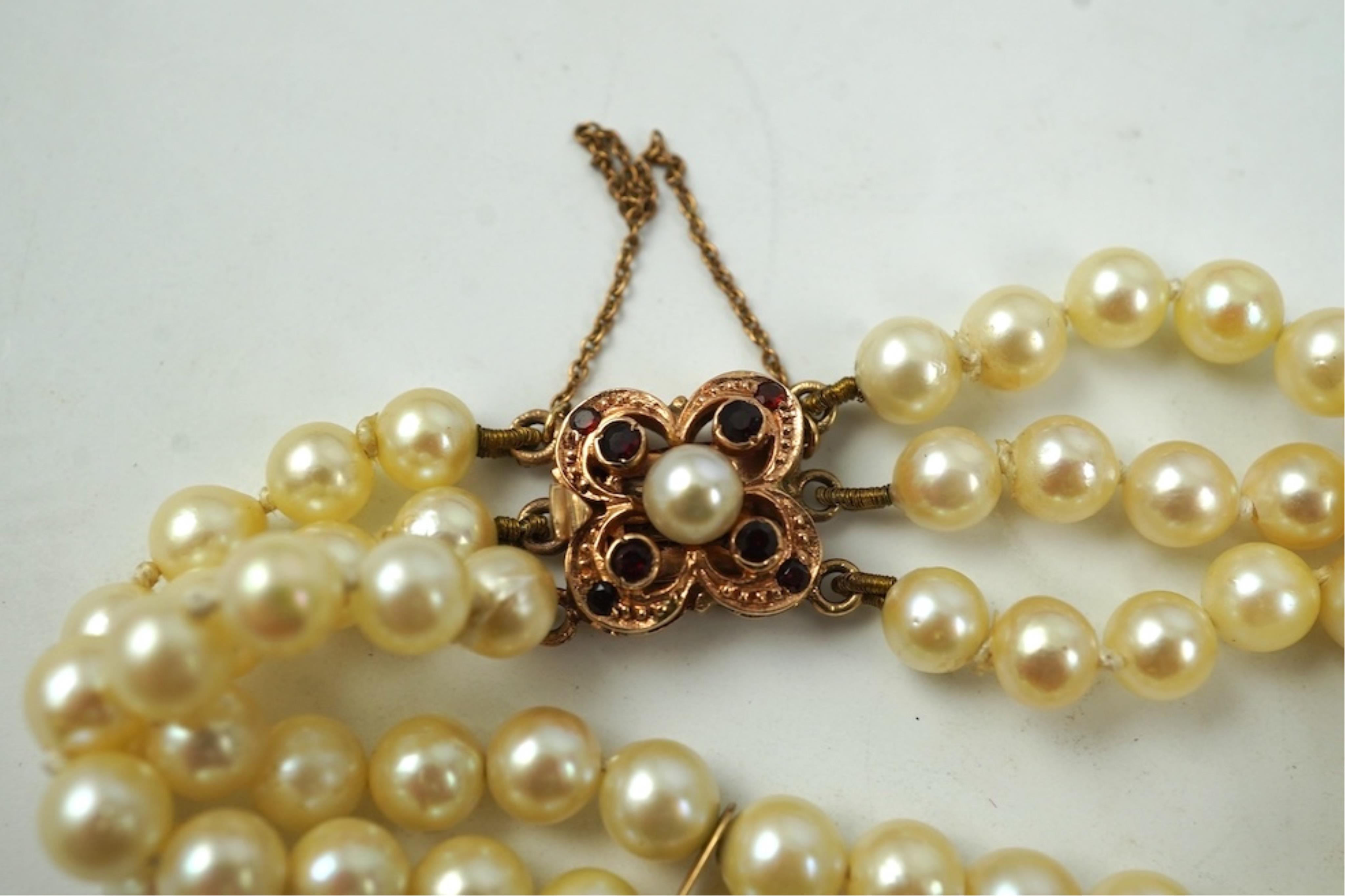 A triple strand cultured pearl bracelet, with a 9ct gold, garnet and cultured pearl cluster set clasp, 16cm.